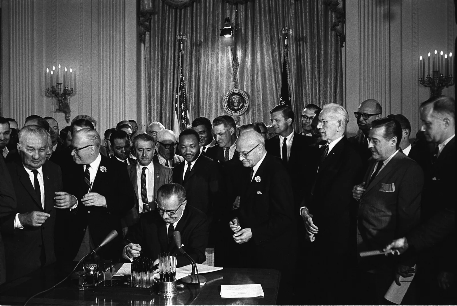 President Lyndon Johnson signing the Civil Rights Act, with Martin Luther King Jr. looking on.